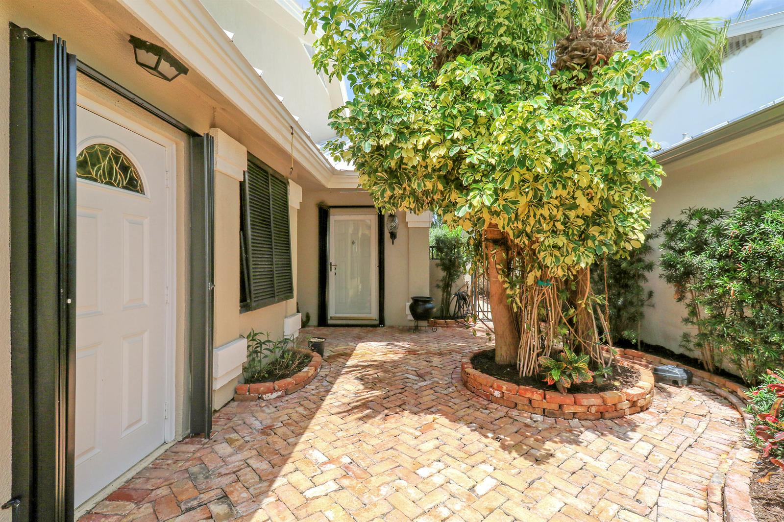 A brick-paved courtyard features a large variegated tree and two white entry doors — 109 Seashore Drive, Jupiter FL 33477, JUPITER, FL