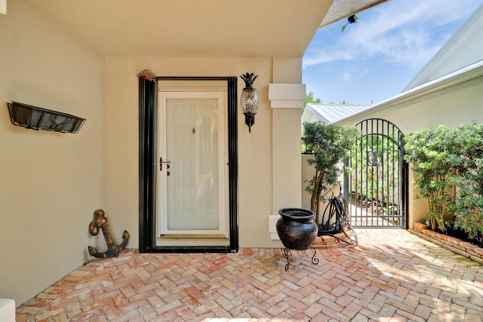 A brick-paved patio features a white door, a black metal gate, and decorative nautical accents — 109 Seashore Drive, Jupiter FL 33477, JUPITER, FL