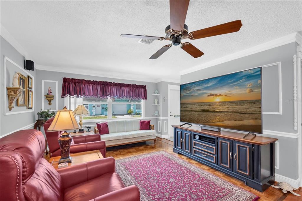 A living room features a large television, red leather chairs, and a patterned area rug — 6915 VERSAILLES N, PINELLAS PARK, FL
