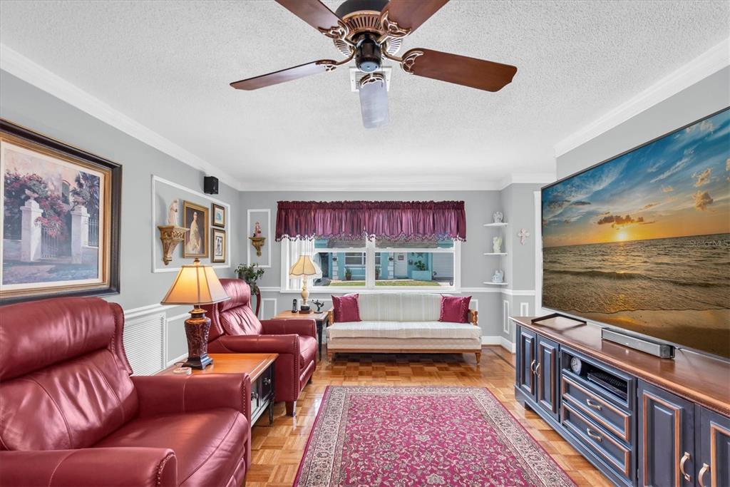 A living room features a red leather recliner, a sofa, a large television, and parquet flooring — 6915 VERSAILLES N, PINELLAS PARK, FL