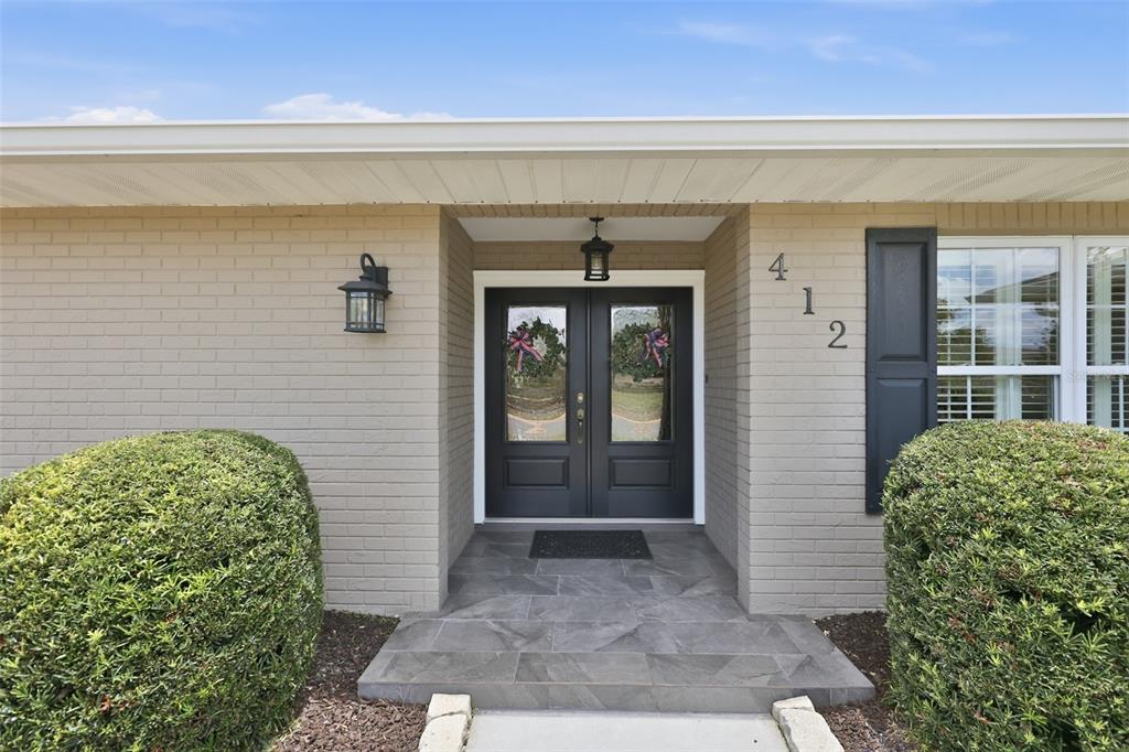 A tan brick house exterior features a dark double front door and gray tiled entryway — 412 STONEHAM DRIVE, SUN CITY CENTER, FL