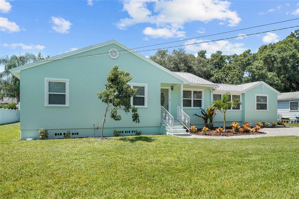 A light green, single-story house with a white front door and a landscaped front yard — 814 W INDIANA AVENUE, TAMPA, FL