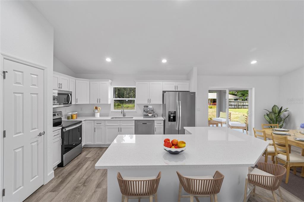 A bright kitchen features white cabinets, stainless steel appliances, a quartz island, and wood-look flooring — 5861 NW 64TH STREET, OCALA, FL