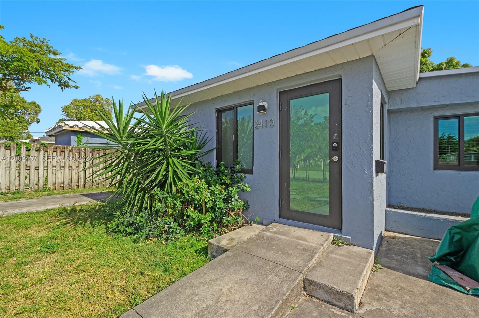 The exterior of a gray house features a glass front door and a concrete walkway — 2410 Jackson St, Hollywood FL 33020, HOLLYWOOD, FL