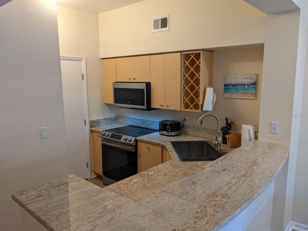 A kitchen features light wood cabinets, granite countertops, stainless steel appliances, and a breakfast bar — 100 4TH AVENUE S UNIT 224, ST PETERSBURG, FL