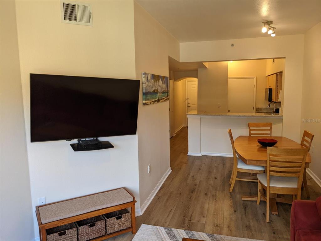 A living room with a wall-mounted television, dining area, and kitchen counter with wood flooring — 100 4TH AVENUE S UNIT 224, ST PETERSBURG, FL