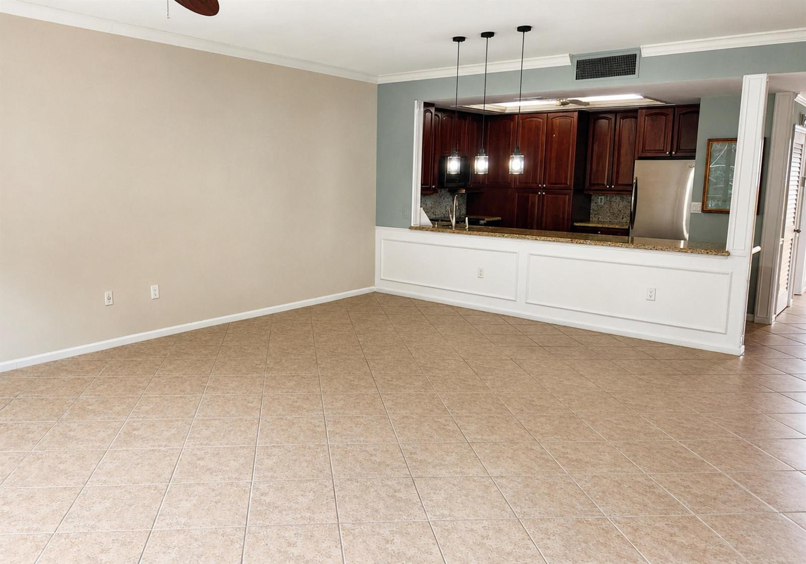 An open-concept living area features tile flooring, a beige wall, and a kitchen pass-through window — 70 Celestial Way # 108, Juno Beach FL 33408, JUNO BEACH, FL