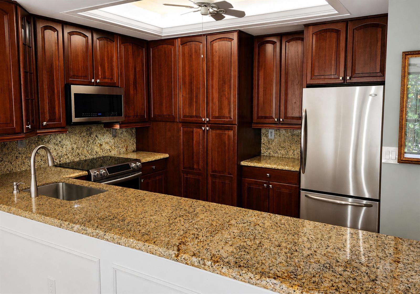 A kitchen with dark wood cabinets, granite countertops, and stainless steel appliances — 70 Celestial Way # 108, Juno Beach FL 33408, JUNO BEACH, FL