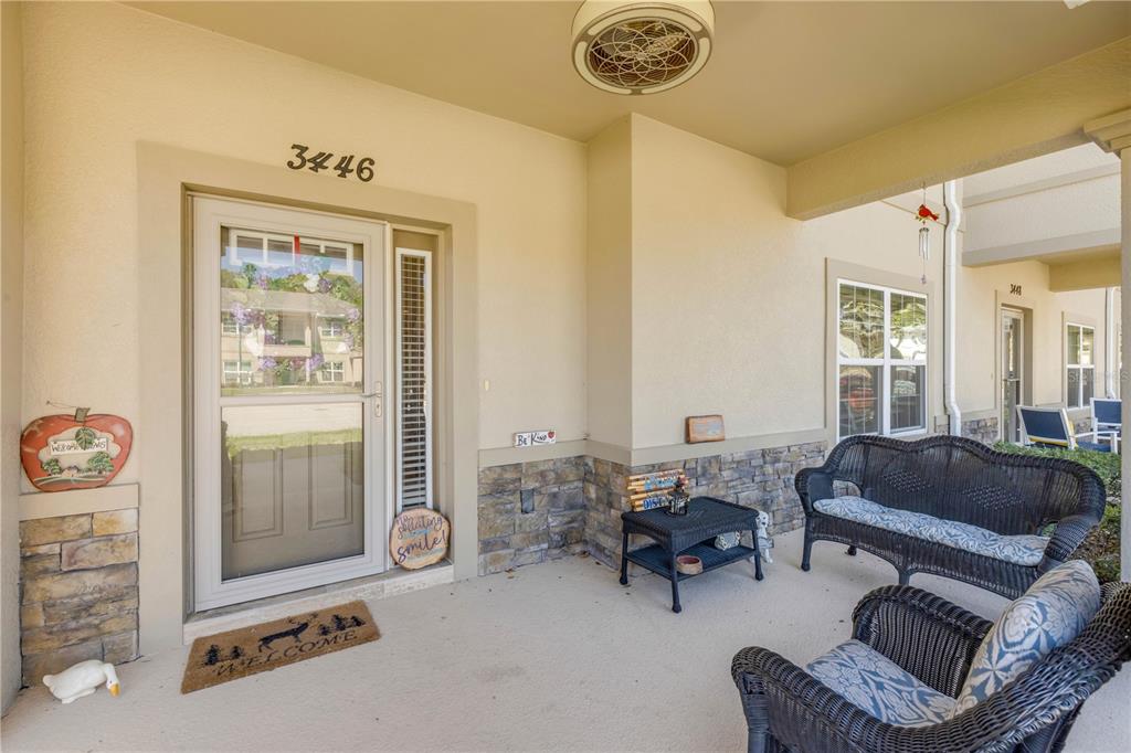 A covered porch features a front door, stone accents, wicker furniture, and a ceiling fan — 3446 MEDICI BOULEVARD, NEW SMYRNA BEACH, FL