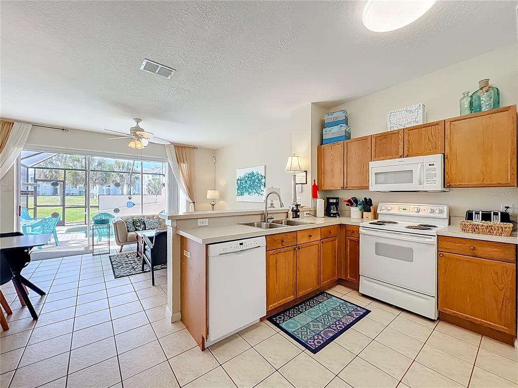 A kitchen with wood cabinets and white appliances opens to a living area with patio access — 8104 PRINCESS PALM LANE, KISSIMMEE, FL