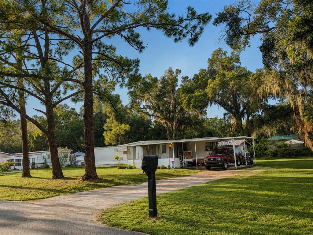 A single-story mobile home with a carport and a red truck sits on a grassy lot — 3323 J AND J MANOR ROAD, LAKELAND, FL