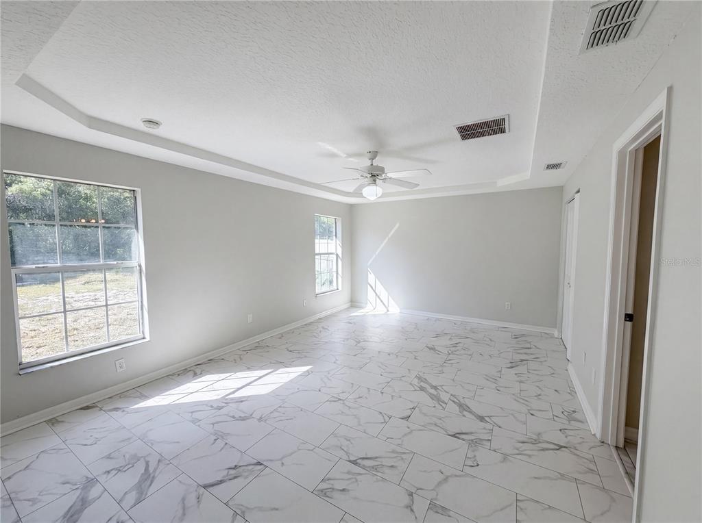 A bedroom with white walls, a tray ceiling, a ceiling fan, and marble-patterned tile flooring — 17052 SW 39TH CIRCLE, OCALA, FL