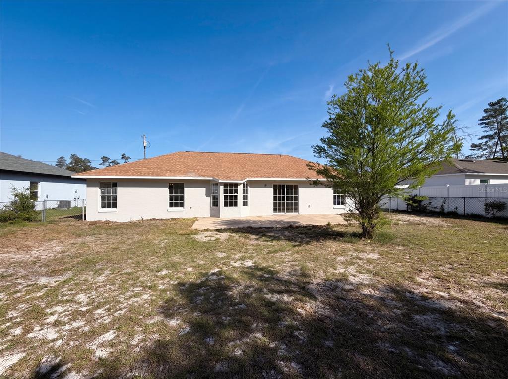 The rear exterior of a single-story house with a light-colored brick facade and yard — 17052 SW 39TH CIRCLE, OCALA, FL
