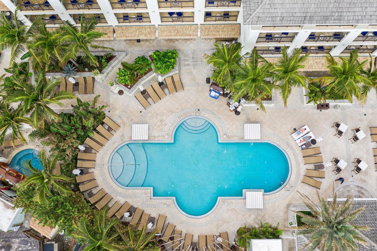 An aerial view shows a resort pool surrounded by lounge chairs, palm trees, and buildings — 3500 Ocean Drive # 228, Vero Beach FL 32963, VERO BEACH, FL
