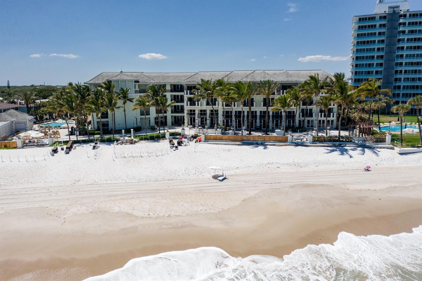An aerial view shows a multi-story beachfront hotel with palm trees and a sandy beach — 3500 Ocean Drive # 228, Vero Beach FL 32963, VERO BEACH, FL