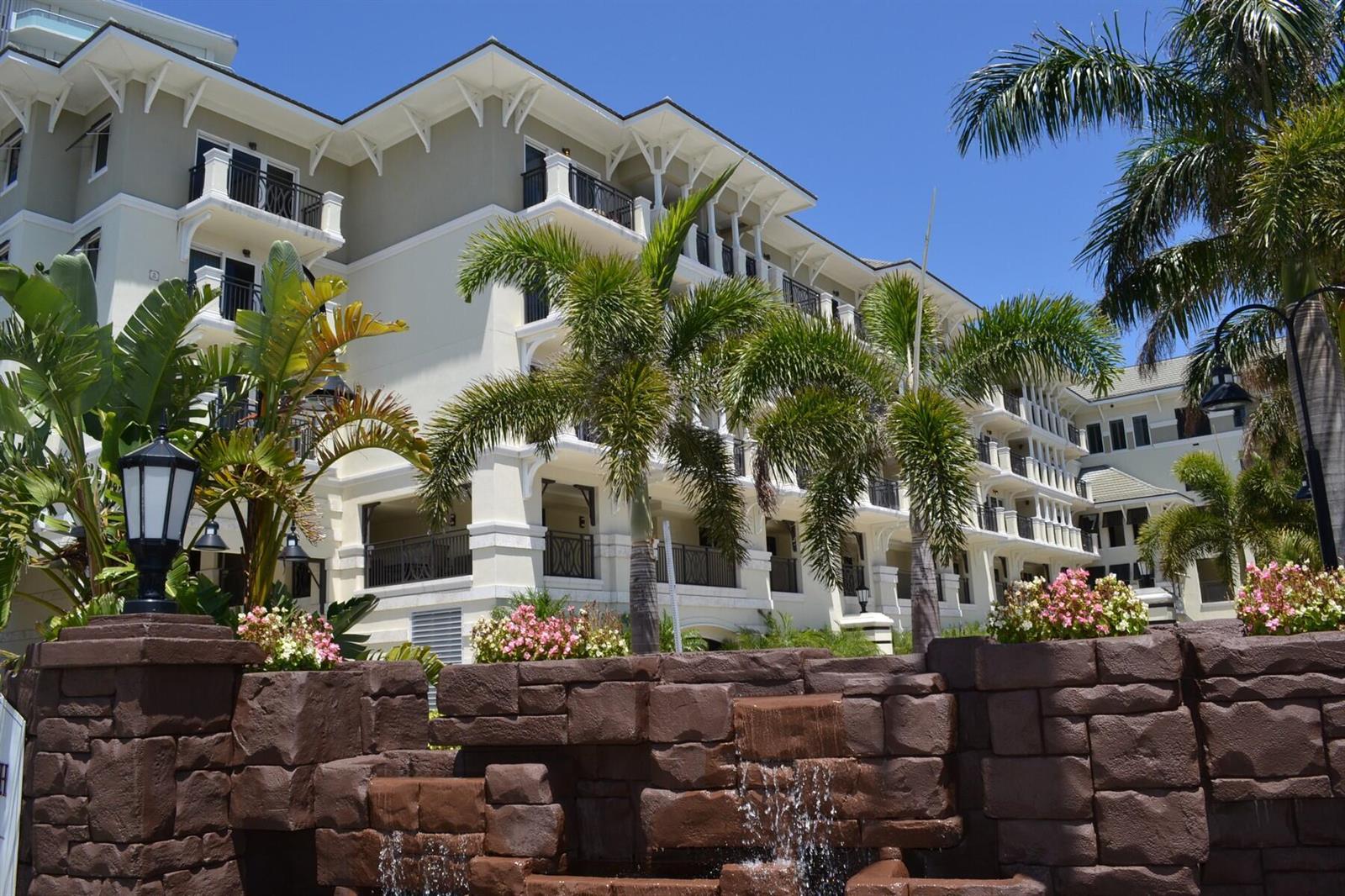 A multi-story building with balconies sits behind a stone fountain and tropical landscaping — 3500 Ocean Drive # 228, Vero Beach FL 32963, VERO BEACH, FL