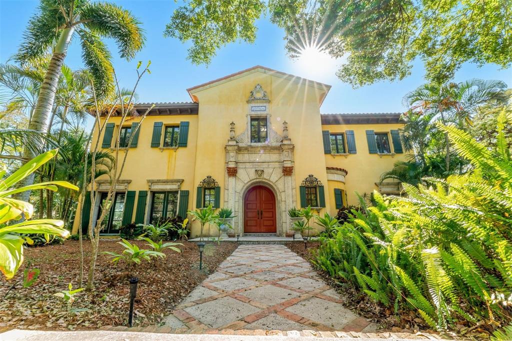 A two-story yellow Mediterranean-style house with a red arched door and a stone walkway — 9340 S TROPICAL TRAIL, MERRITT ISLAND, FL
