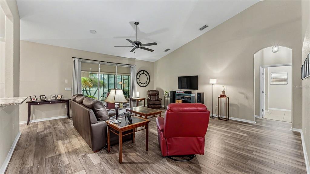 A living room features wood-look flooring, a vaulted ceiling, a ceiling fan, and red furniture — 2985 VINTAGE VIEW CIRCLE, LAKELAND, FL
