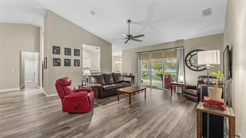 A living room features wood-look flooring, a vaulted ceiling, a red recliner, and sliding glass doors — 2985 VINTAGE VIEW CIRCLE, LAKELAND, FL