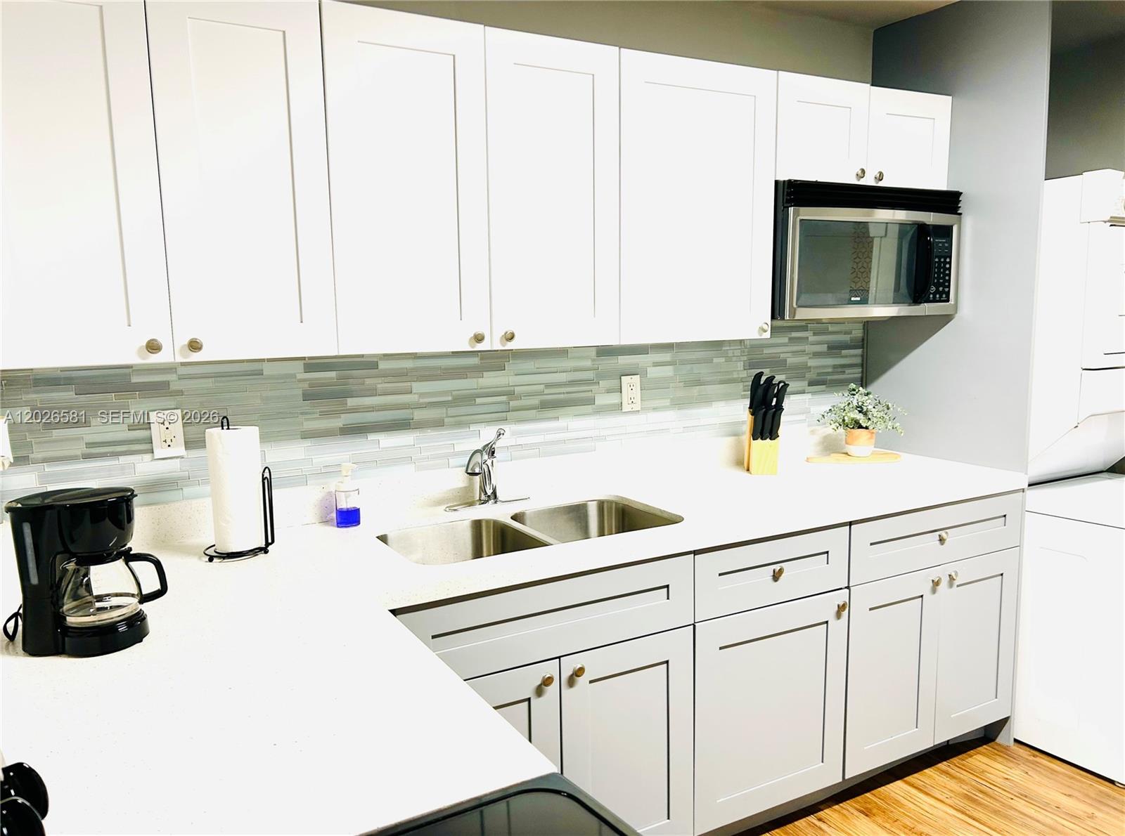 A kitchen features white upper cabinets, light gray lower cabinets, and a glass tile backsplash — 1011 NW 7th Ave # 1011, Miami FL 33136, MIAMI, FL