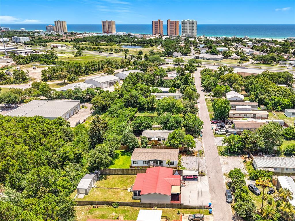 An aerial view shows a house with a red roof, surrounding trees, and distant oceanfront buildings — 128 N VESTAVIA STREET, PANAMA CITY BEACH, FL