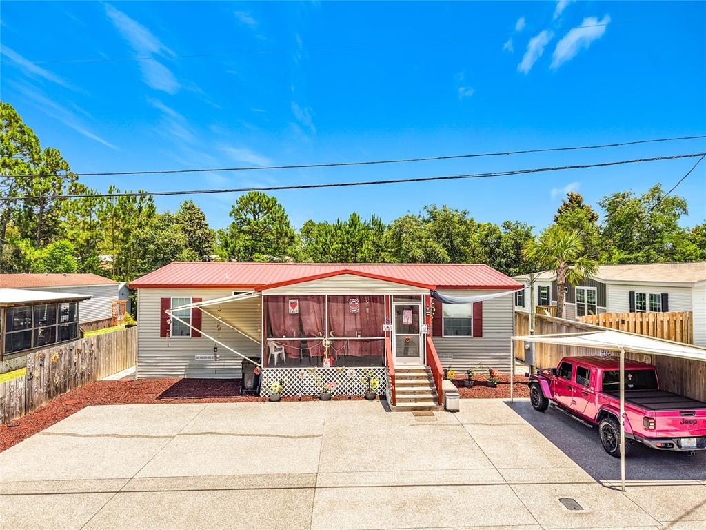 A single-story manufactured home with a red metal roof, screened porch, and concrete driveway — 128 N VESTAVIA STREET, PANAMA CITY BEACH, FL