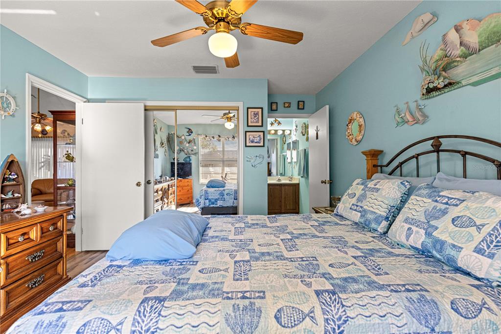 A bedroom features light blue walls, a patterned quilt, a ceiling fan, and mirrored closet doors — 11255 SE 175TH LN, SUMMERFIELD, FL