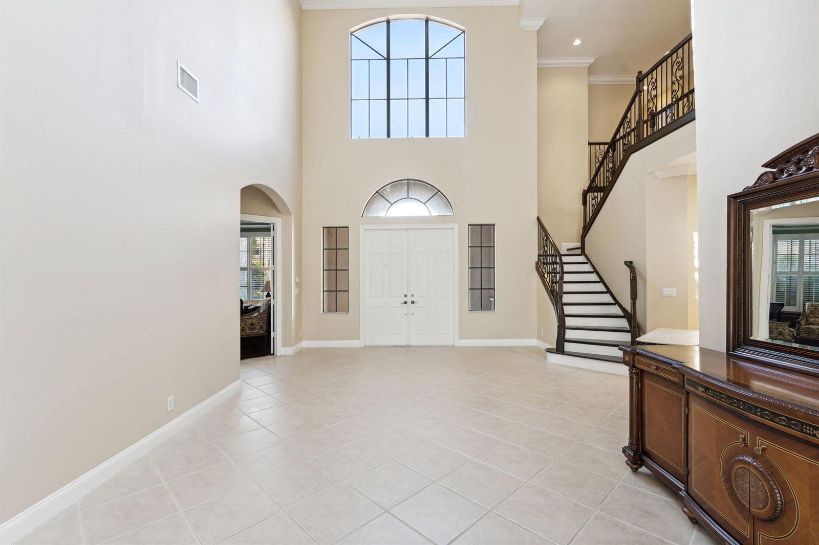 A two-story foyer features tile flooring, a grand staircase, and a large arched window — 10380 Trianon Place, Wellington FL 33449, WELLINGTON, FL