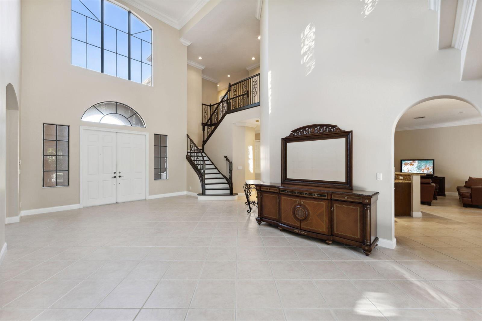 A spacious foyer features tile flooring, a grand staircase, and a large wooden console table — 10380 Trianon Place, Wellington FL 33449, WELLINGTON, FL
