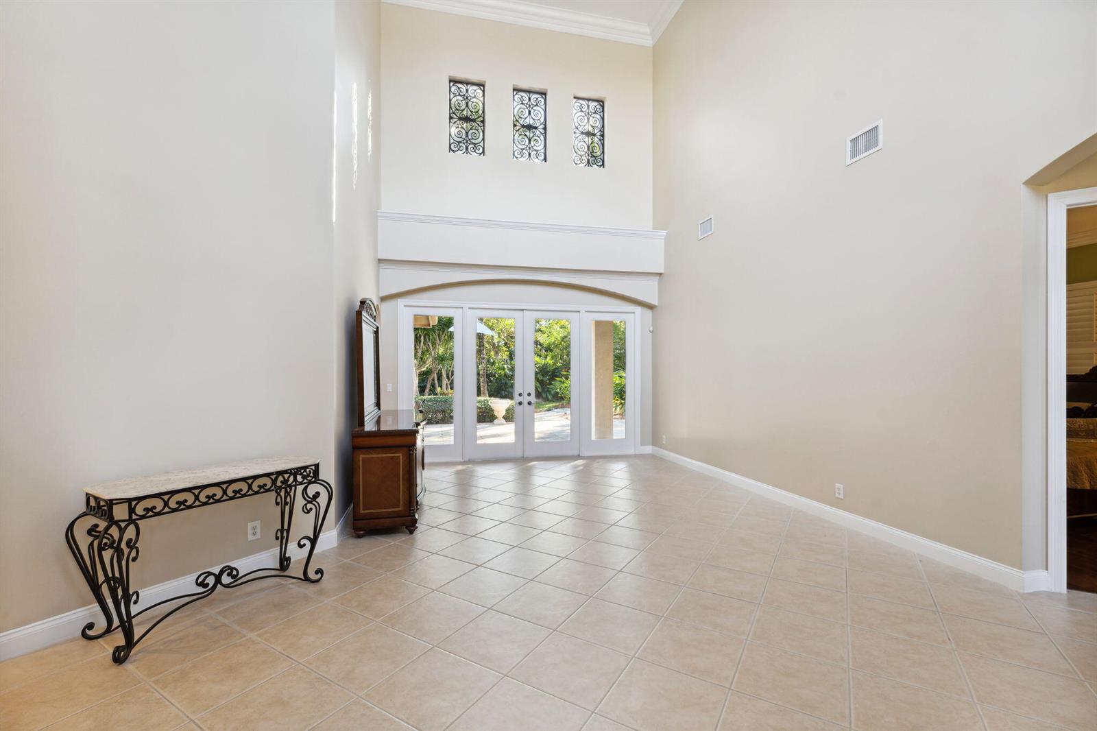 A spacious room with high ceilings, tile flooring, and glass doors leading to a patio — 10380 Trianon Place, Wellington FL 33449, WELLINGTON, FL