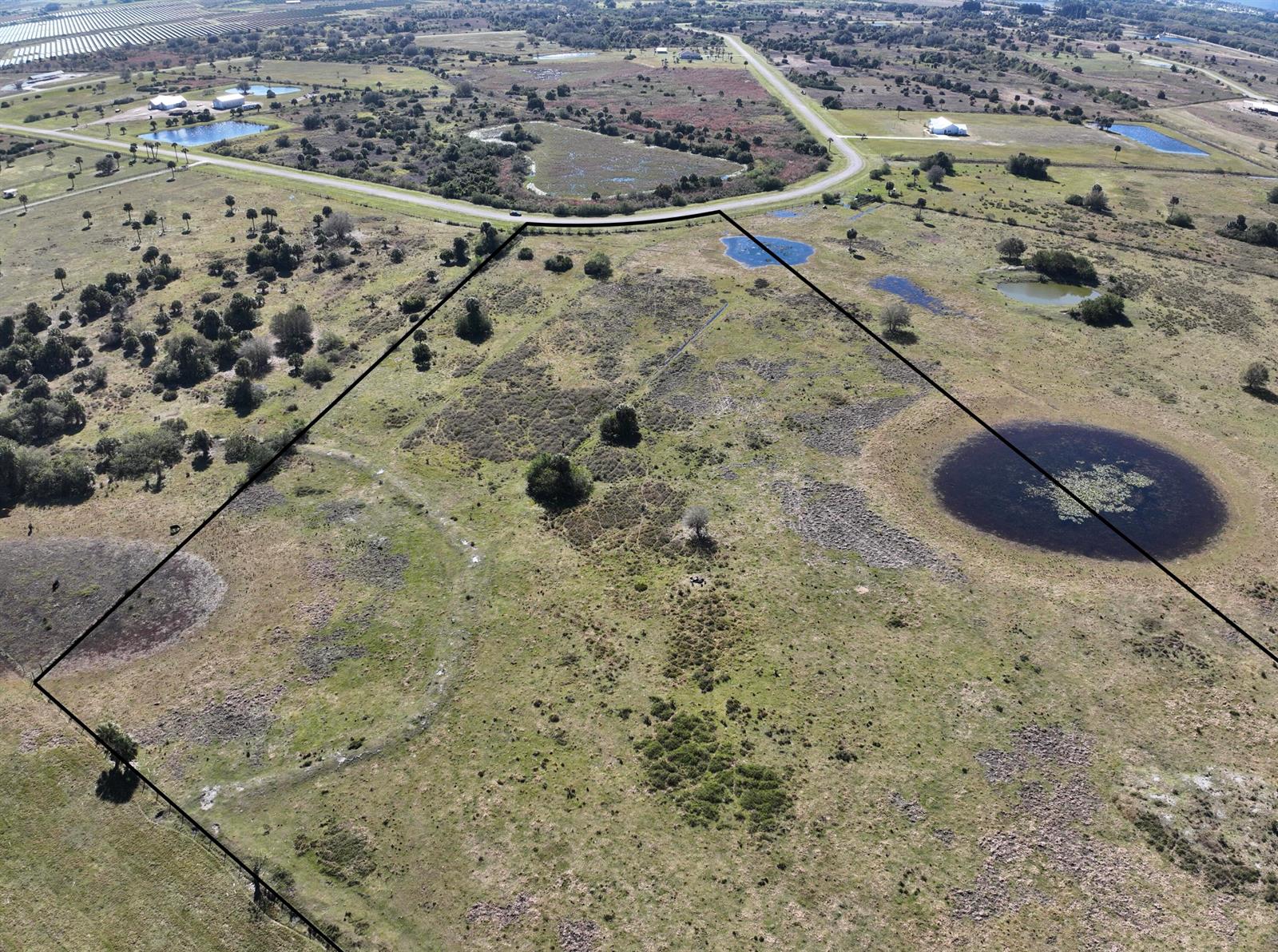An aerial view shows a large, grassy plot of land outlined in black with ponds — 6572 SE 26th Trail, Okeechobee FL 34974, OKEECHOBEE, FL