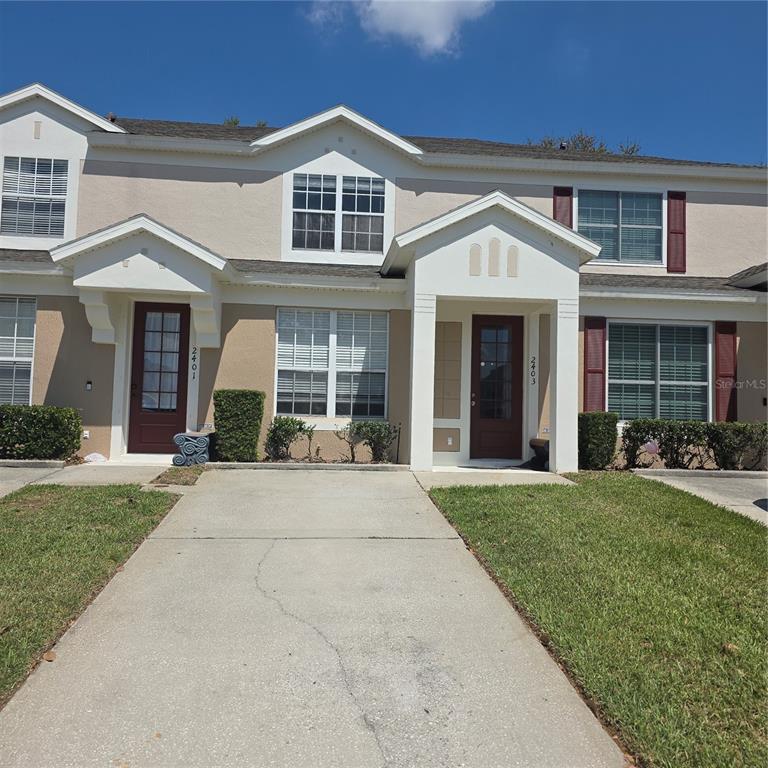 A two-story townhouse exterior with beige stucco, dark red doors, and a concrete driveway — 2403 SILVER PALM DRIVE, KISSIMMEE, FL