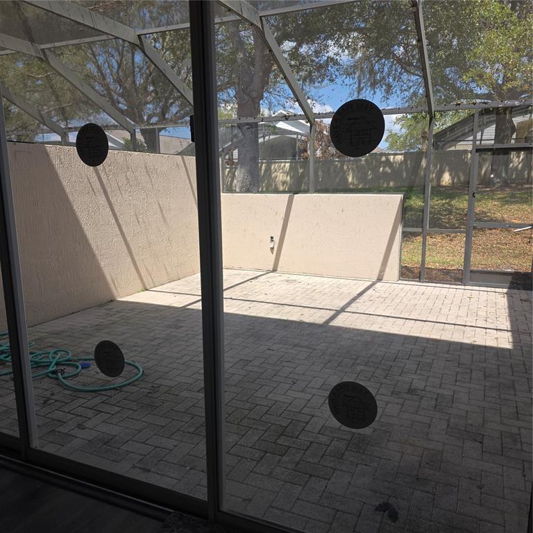 A screened-in patio features paver flooring and beige privacy walls viewed through sliding glass doors — 2403 SILVER PALM DRIVE, KISSIMMEE, FL