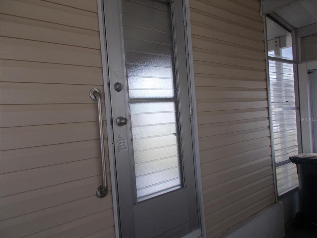 A metal storm door with a grab bar is mounted on a beige vinyl-sided wall — 6821 OCEAN COURT, NORTH PORT, FL