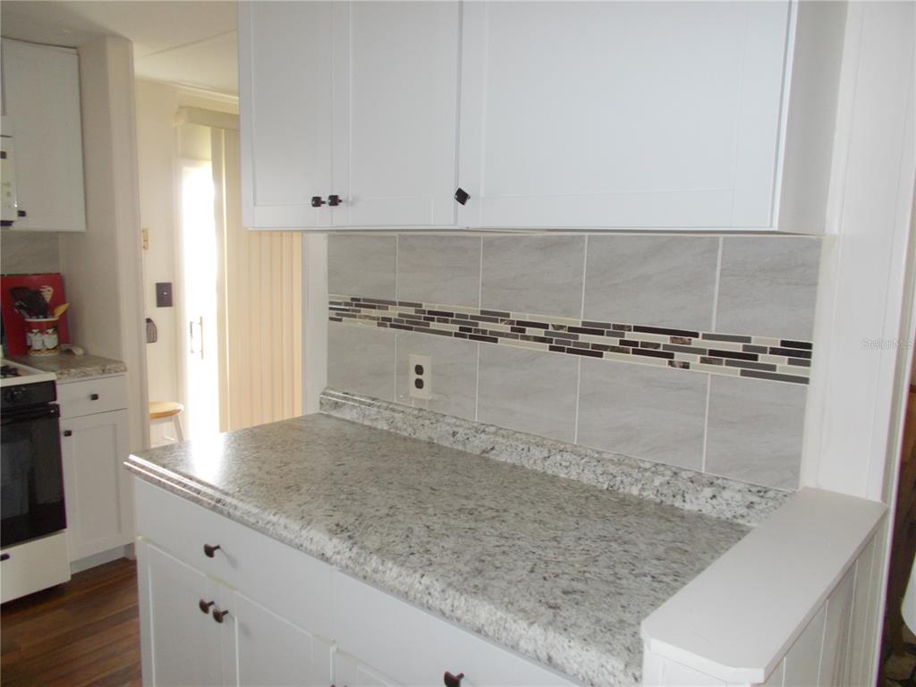 A kitchen features white cabinets, granite countertops, and a gray tiled backsplash with mosaic accents — 6821 OCEAN COURT, NORTH PORT, FL