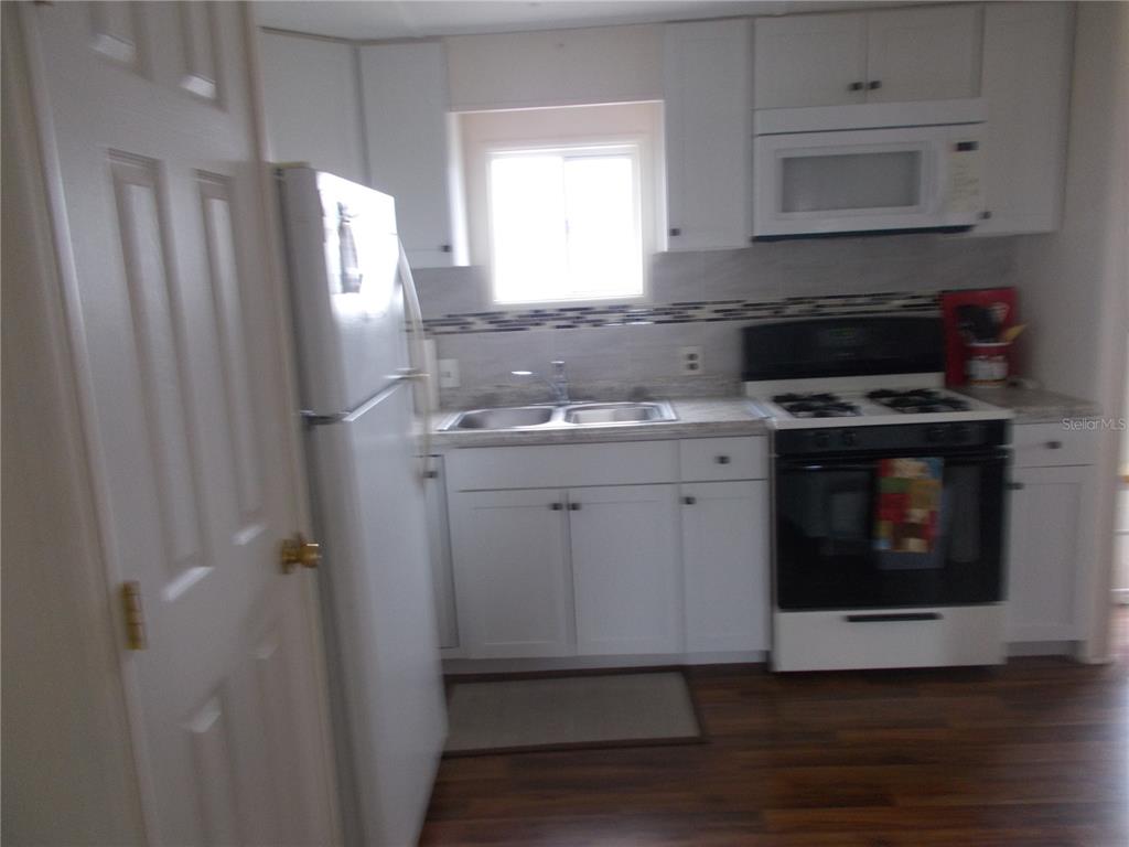 A kitchen features white cabinets, white appliances, a double sink, and dark wood-look flooring — 6821 OCEAN COURT, NORTH PORT, FL