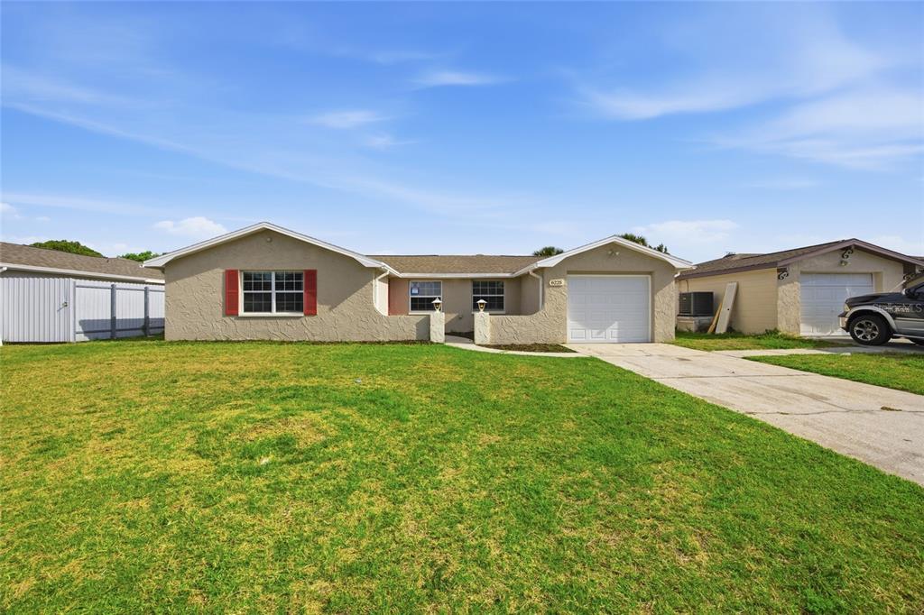 A single-story house with a beige stucco exterior, a front-facing garage, and a large lawn — 6225 WESTPORT DRIVE, PORT RICHEY, FL