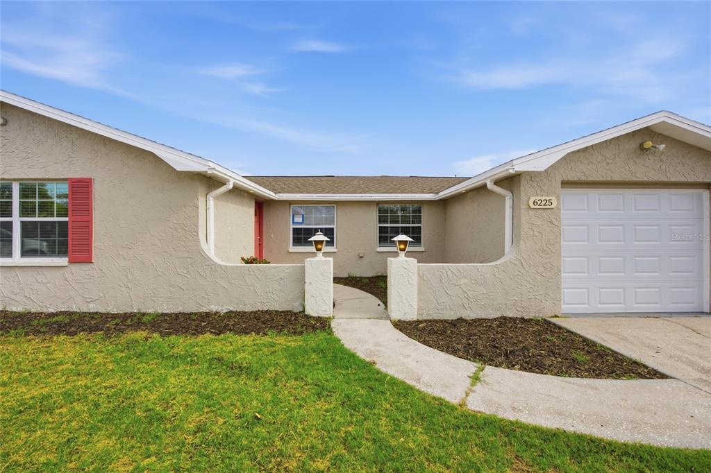 A single-story house exterior features a beige stucco facade, red shutters, and a white garage — 6225 WESTPORT DRIVE, PORT RICHEY, FL