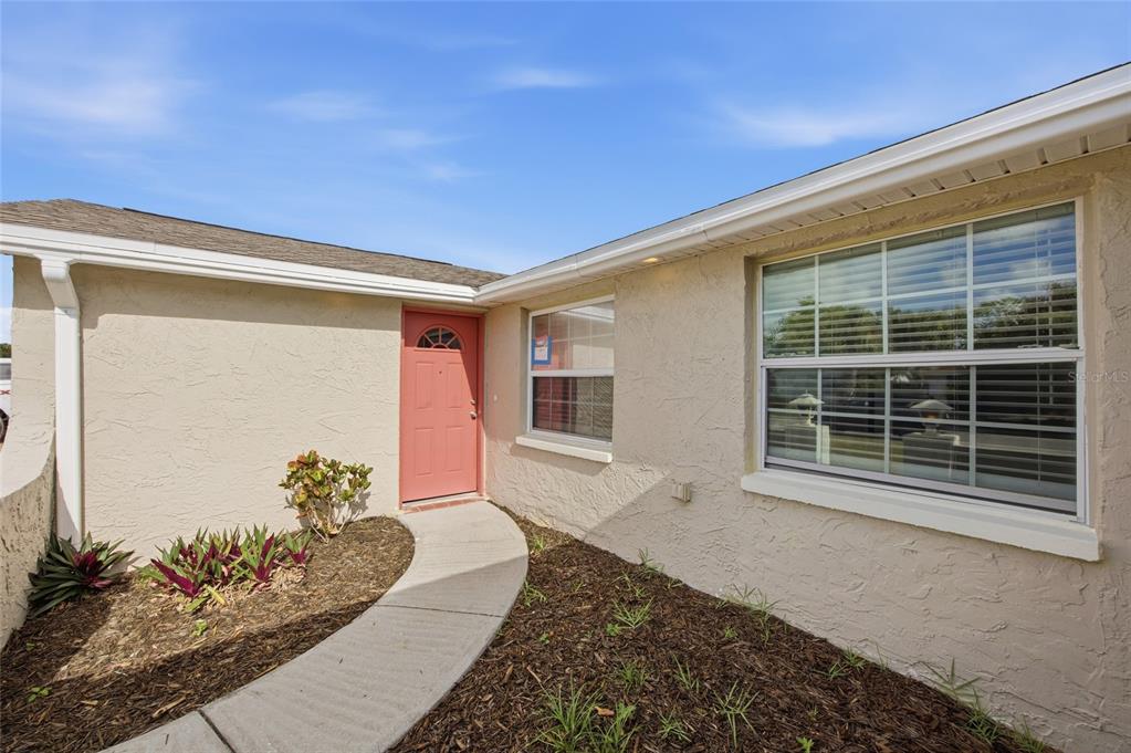 The exterior of a beige stucco house features a red front door and a walkway — 6225 WESTPORT DRIVE, PORT RICHEY, FL