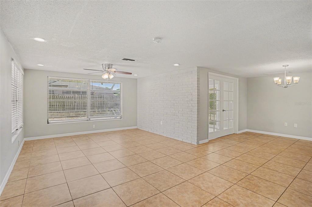 A spacious room with light-colored tile flooring, a white brick accent wall, and French doors — 8006 MIMOSA DRIVE, PORT RICHEY, FL