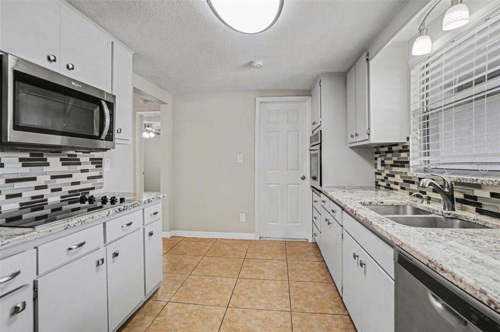 A kitchen with white cabinets, granite countertops, stainless steel appliances, and tiled flooring — 8006 MIMOSA DRIVE, PORT RICHEY, FL