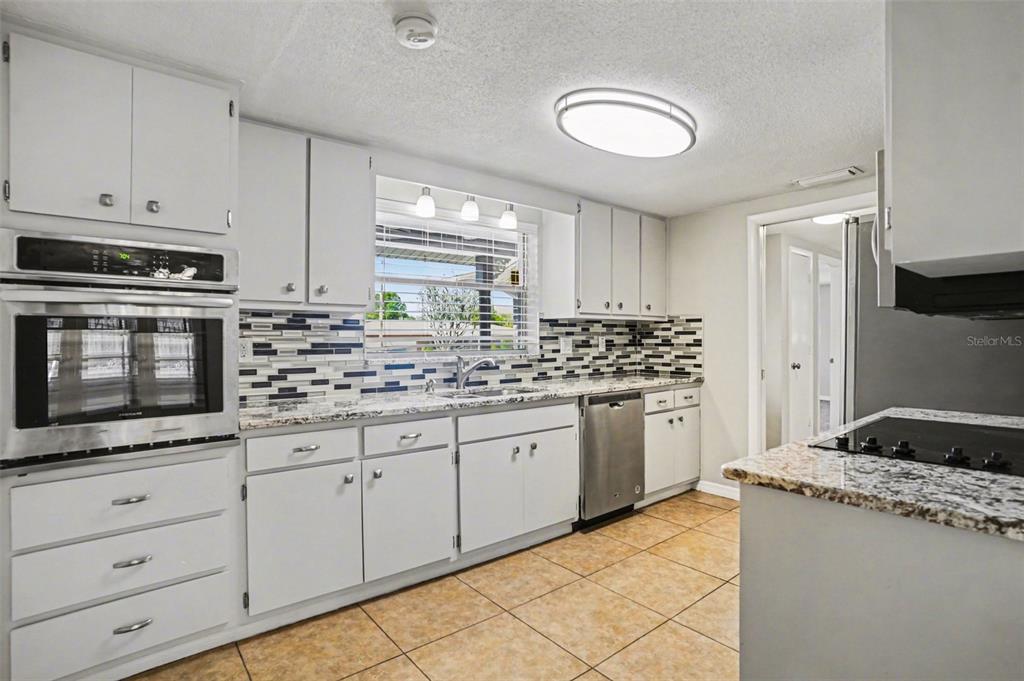 A kitchen features white cabinets, granite countertops, a tiled backsplash, and stainless steel appliances — 8006 MIMOSA DRIVE, PORT RICHEY, FL