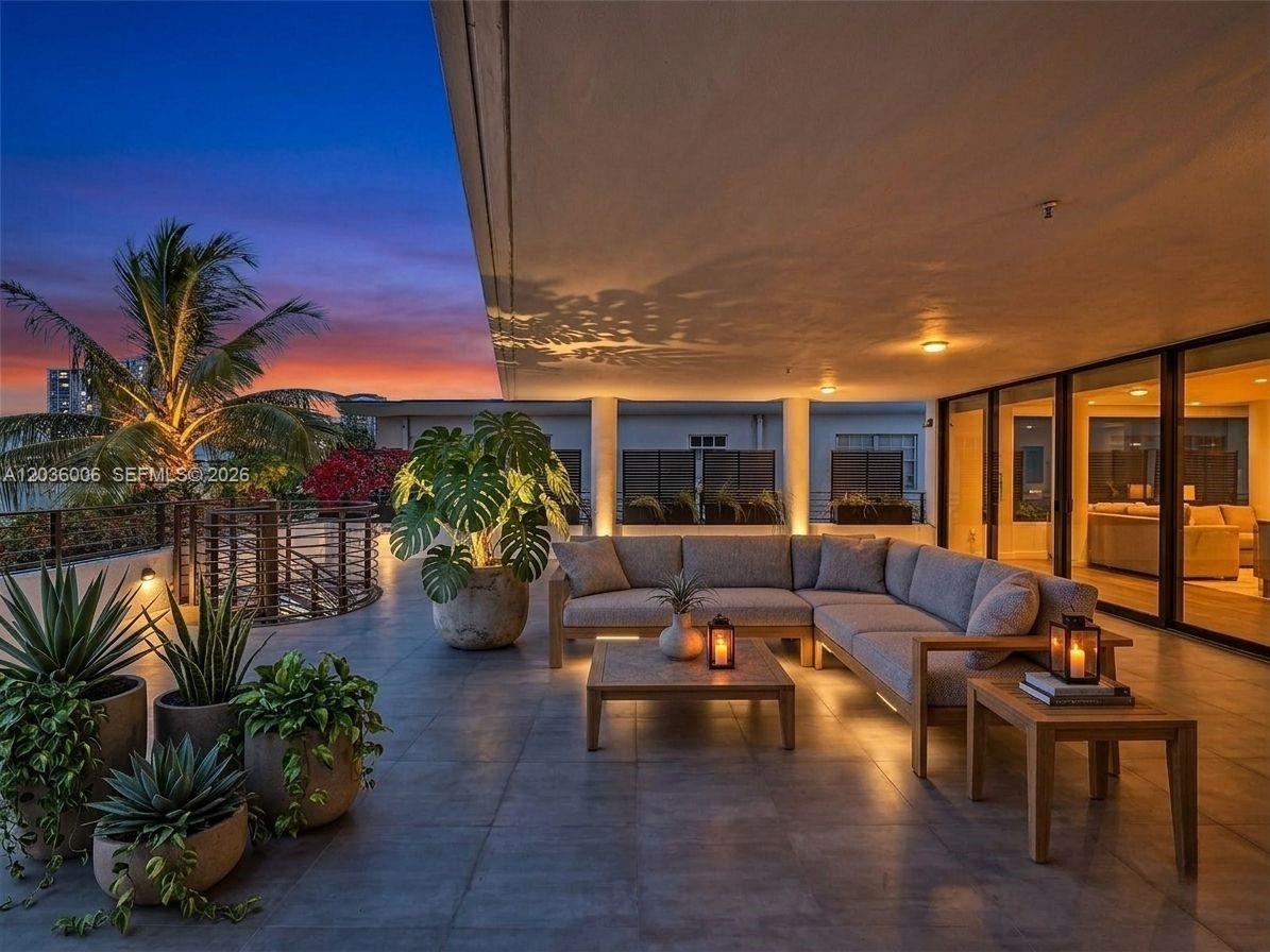 A modern outdoor terrace features a sectional sofa, coffee tables, and potted plants at sunset — 1930 Bay Dr, Miami Beach FL 33141, MIAMI BEACH, FL