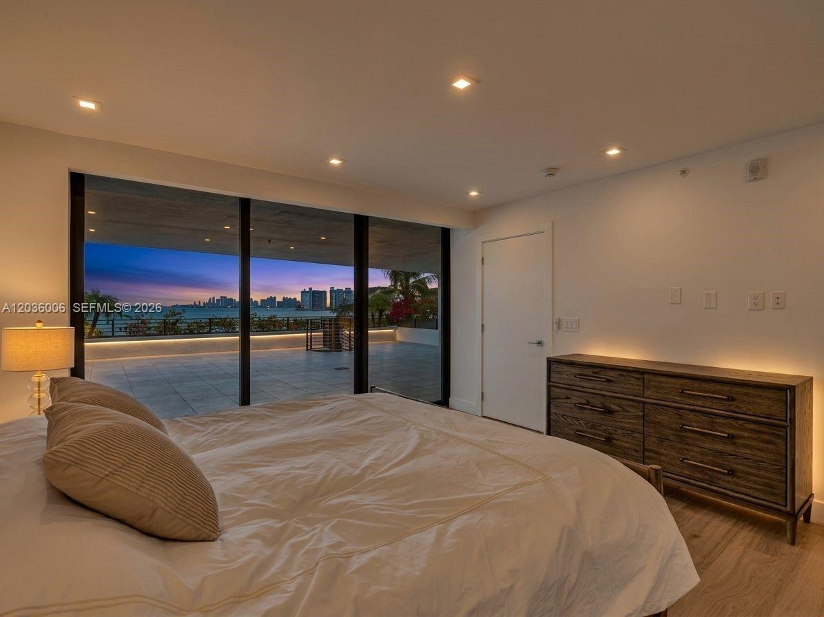 A bedroom features a large bed, a wooden dresser, and floor-to-ceiling windows overlooking a balcony — 1930 Bay Dr, Miami Beach FL 33141, MIAMI BEACH, FL