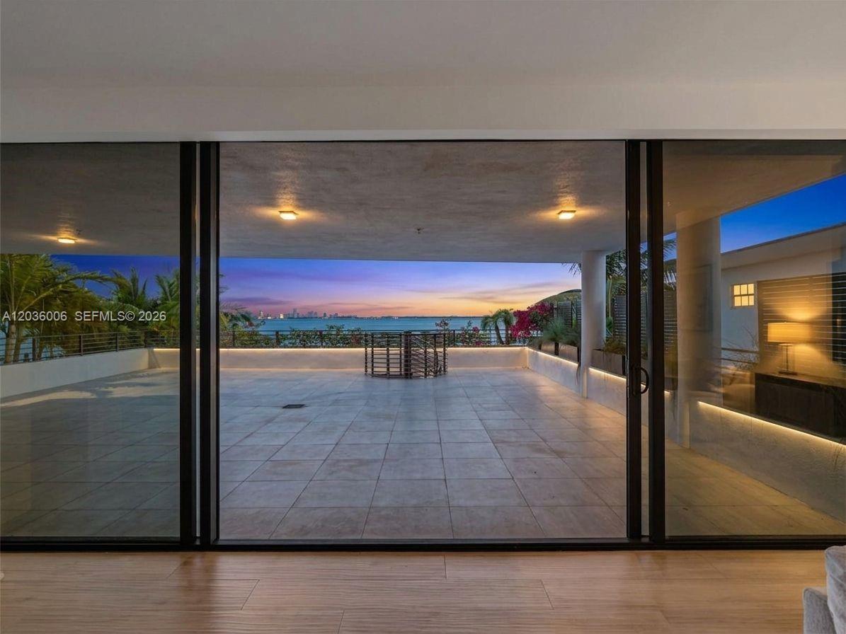 A view from inside a room looking out onto a large tiled balcony overlooking water — 1930 Bay Dr, Miami Beach FL 33141, MIAMI BEACH, FL