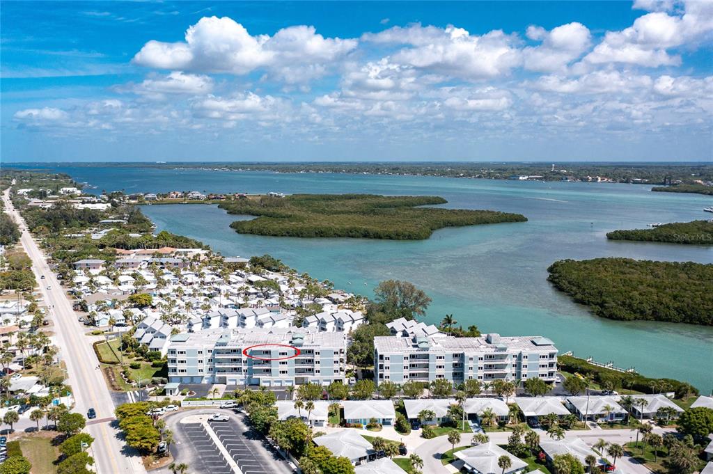An aerial view shows a multi-story apartment complex near a bay with mangroves — 2225 N BEACH ROAD UNIT 402, ENGLEWOOD, FL