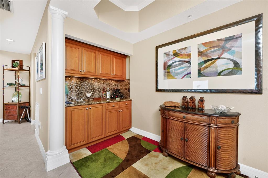 A wet bar with wood cabinets and a mosaic backsplash sits next to a console table — 2225 N BEACH ROAD UNIT 402, ENGLEWOOD, FL