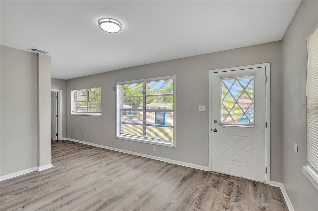 A living room with light gray walls, wood-look flooring, two windows, and a white door — 7015 FILBERT LANE, TAMPA, FL