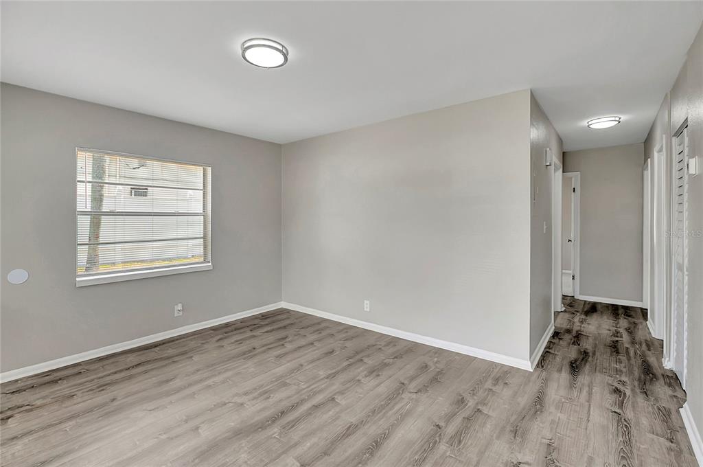 An empty room with gray walls, wood-look flooring, a window with blinds, and ceiling lights — 7015 FILBERT LANE, TAMPA, FL