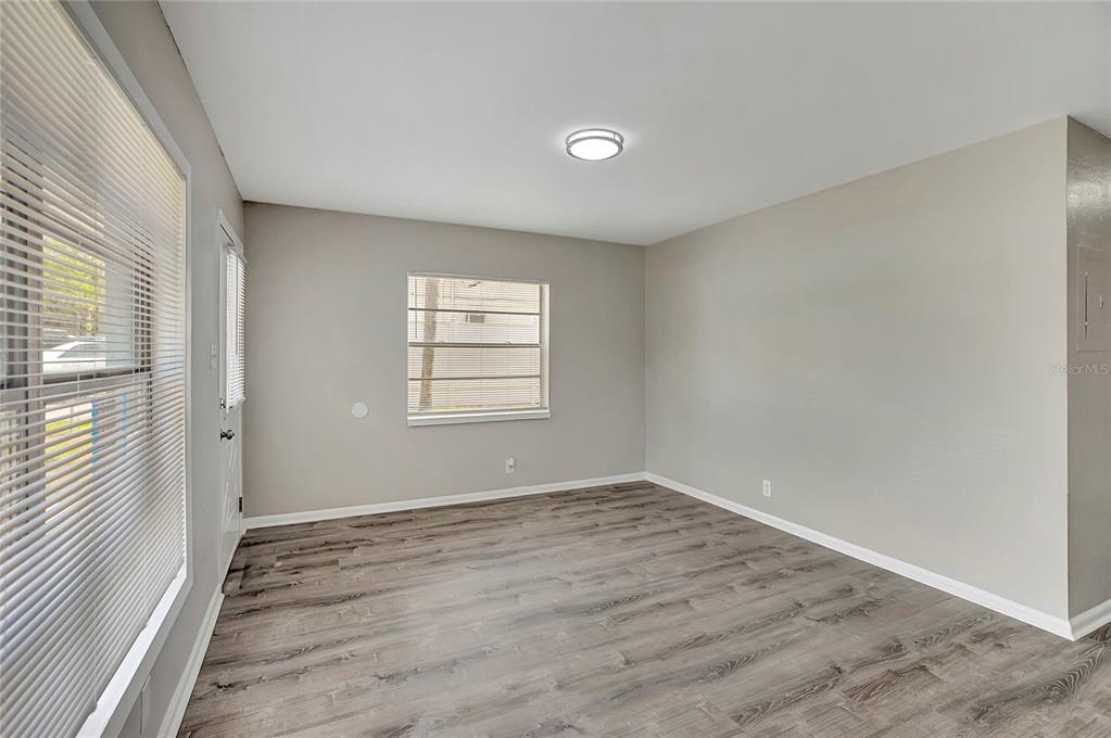 An empty room features light gray walls, wood-look flooring, a ceiling light, and two windows — 7015 FILBERT LANE, TAMPA, FL